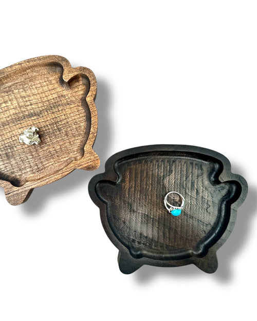 Two wooden ring trays in a cauldron shape, one light brown and one dark brown, shown on a white background with jewelry props.