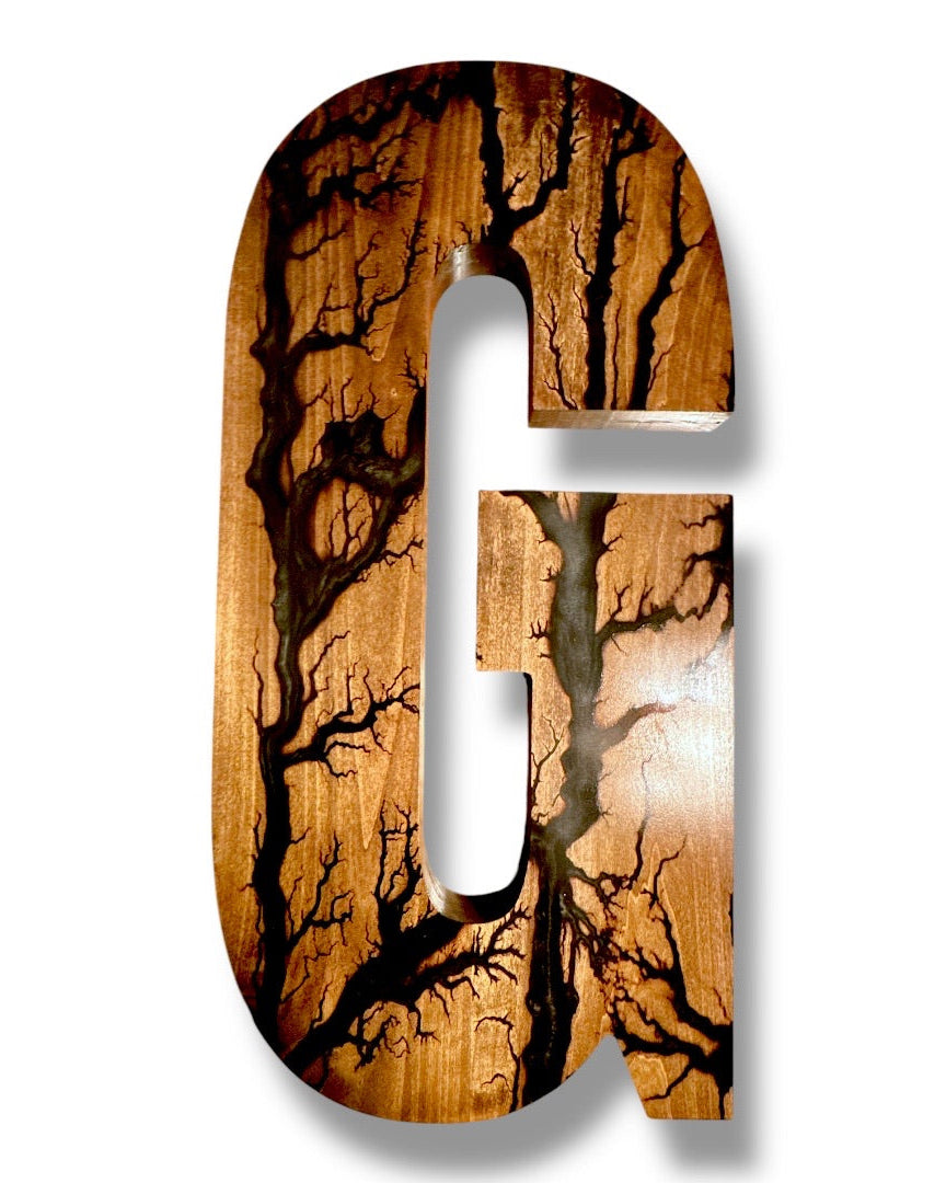A decorative capital letter G made from walnut wood with dramatic dark tree-branch fractal burned grain patterns, shown on a plain white background.