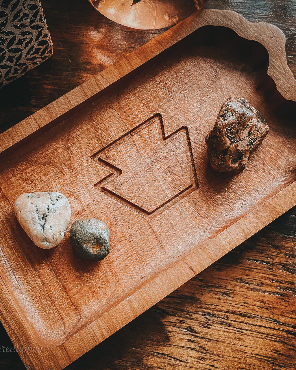 A rectangular PA state tray with a scalloped edge and a carved geometric keystone in the center, styled on a dark wooden table with small stones placed inside.