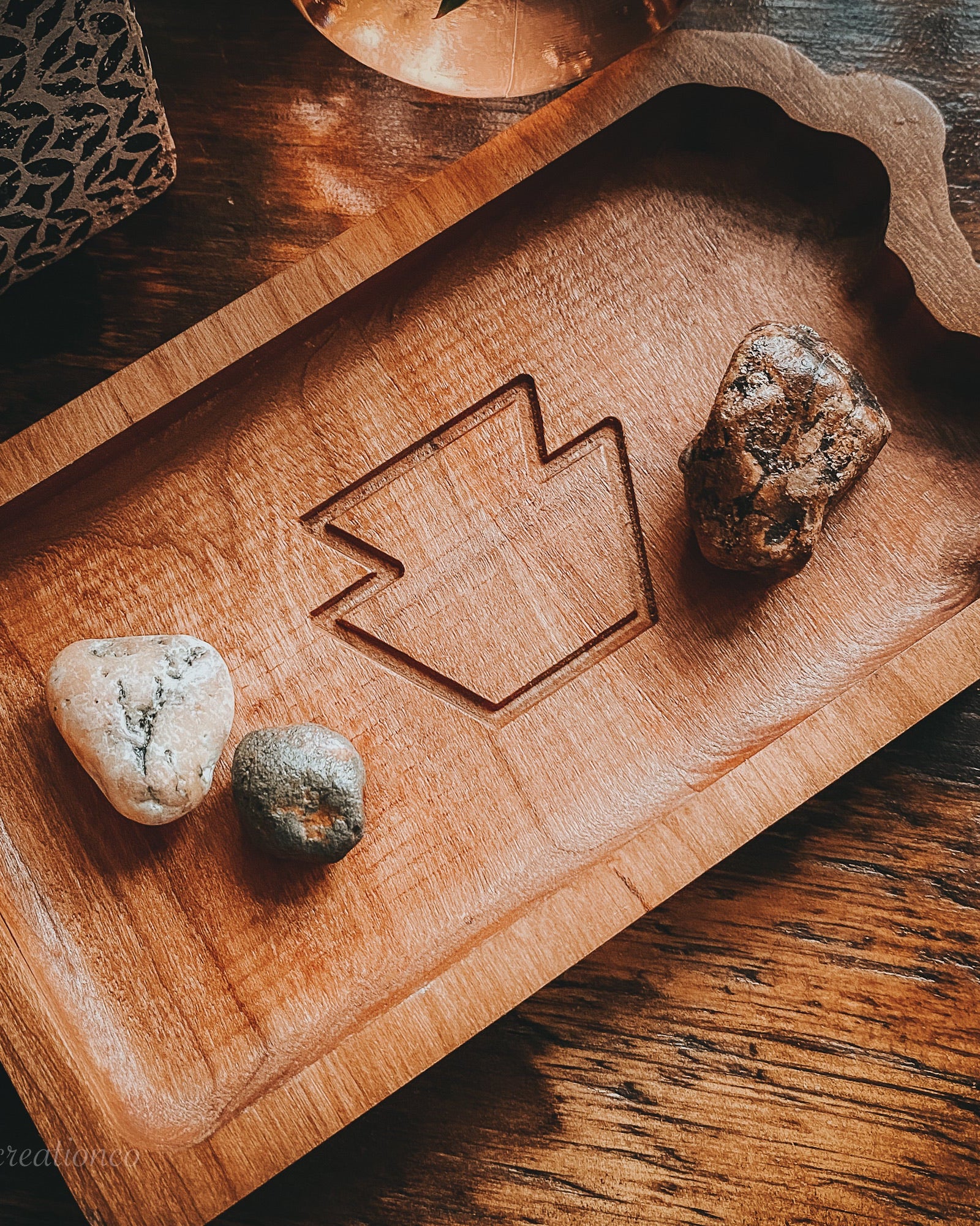 A rectangular PA state tray with a scalloped edge and a carved geometric keystone in the center, styled on a dark wooden table with small stones placed inside.