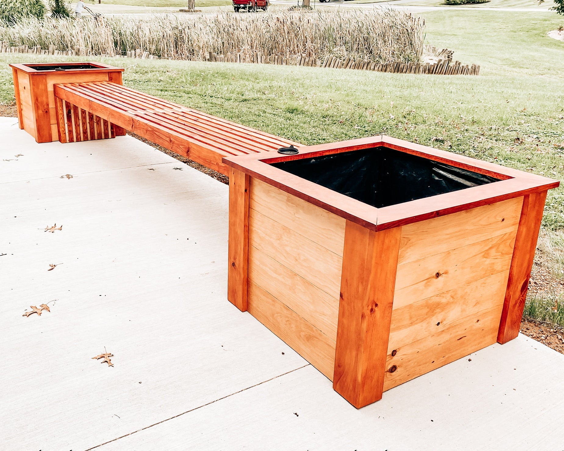 Wooden planter boxes on a concrete surface with grass and plants in the background.