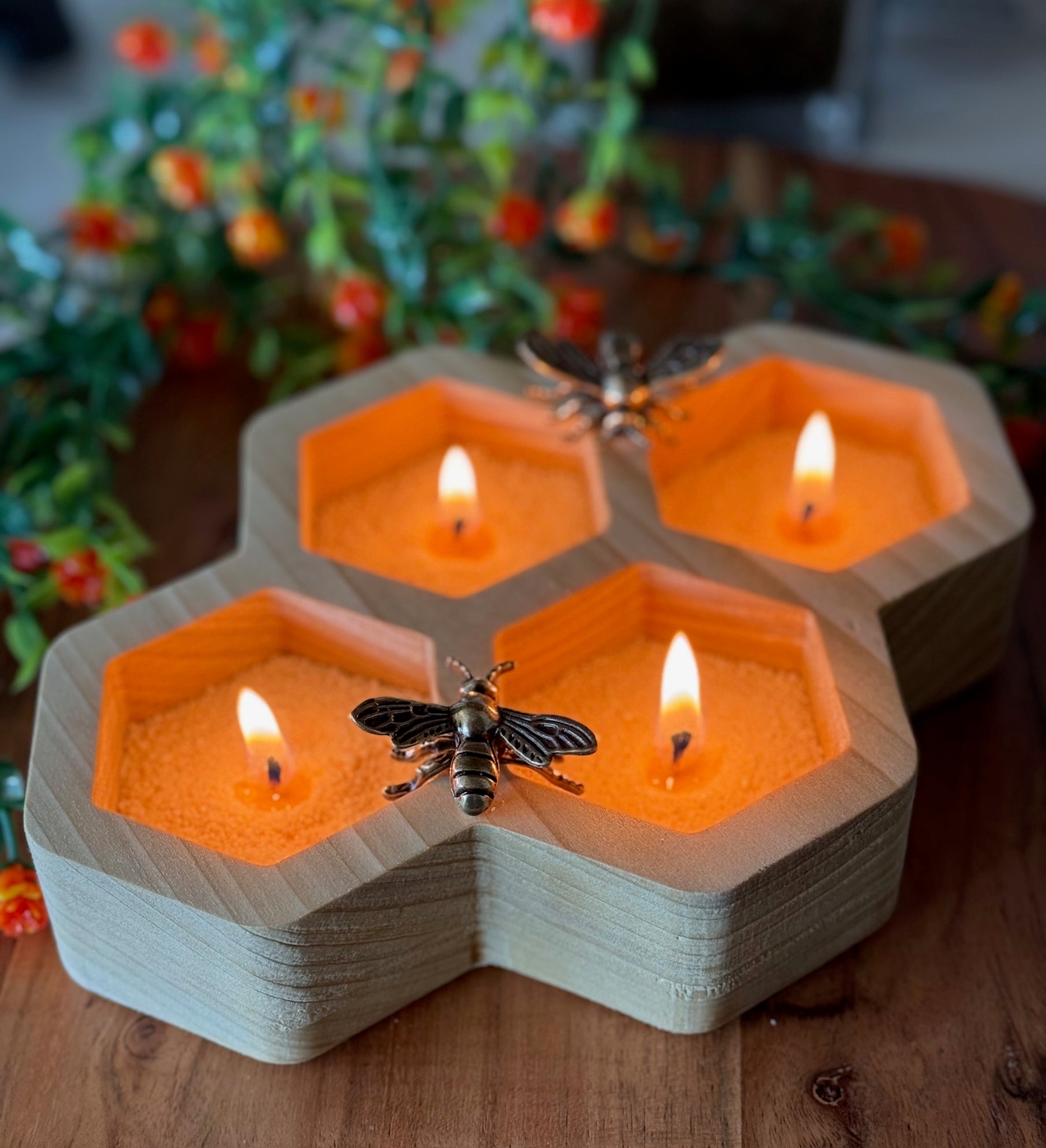 Hexagonal candle wax holders with bees and lit candles on a wooden surface.