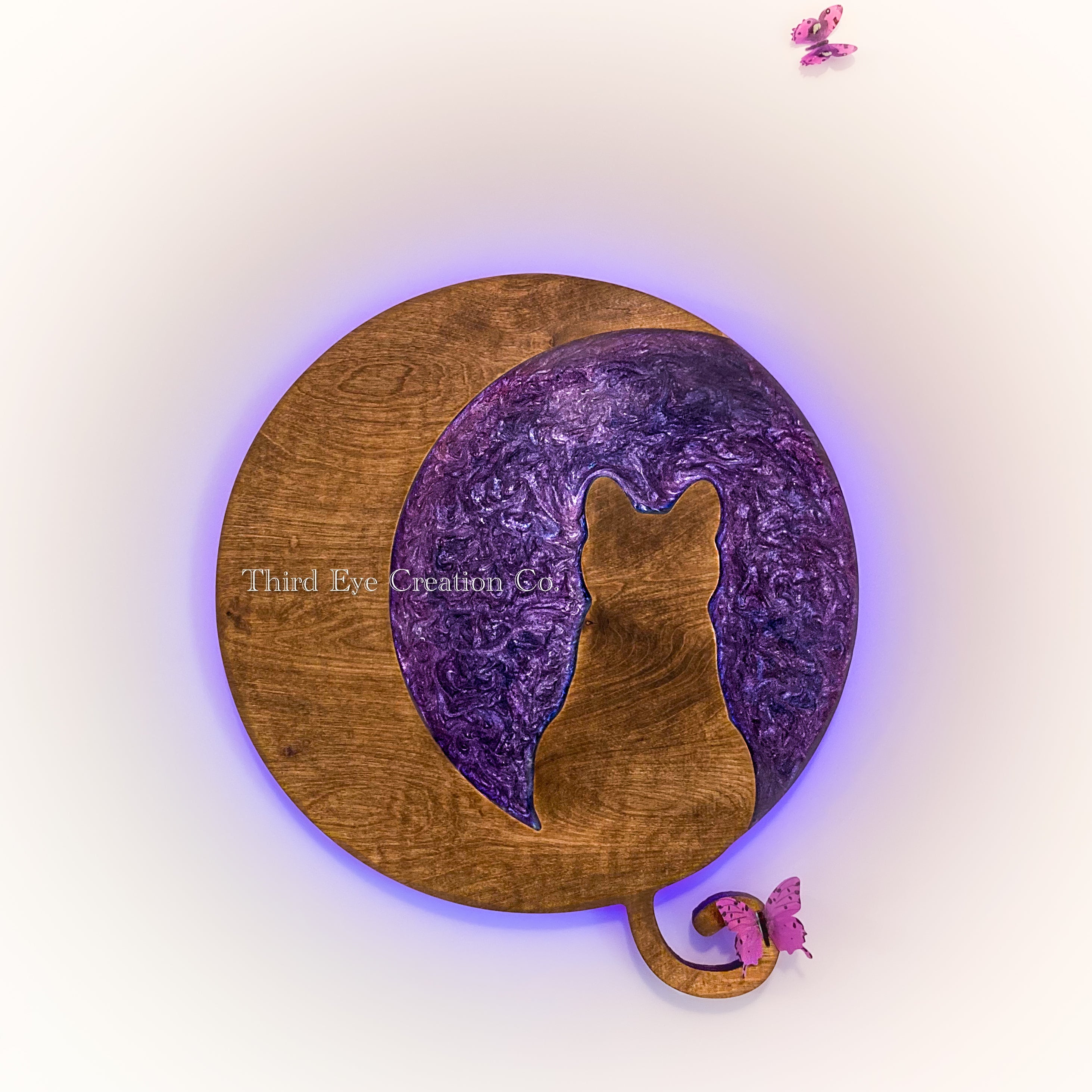 A circular wooden wall art piece featuring a cutout silhouette of a cat over a purple marbled pattern, with a small butterfly accent at the tail end, shown on a white background with a purple glow.