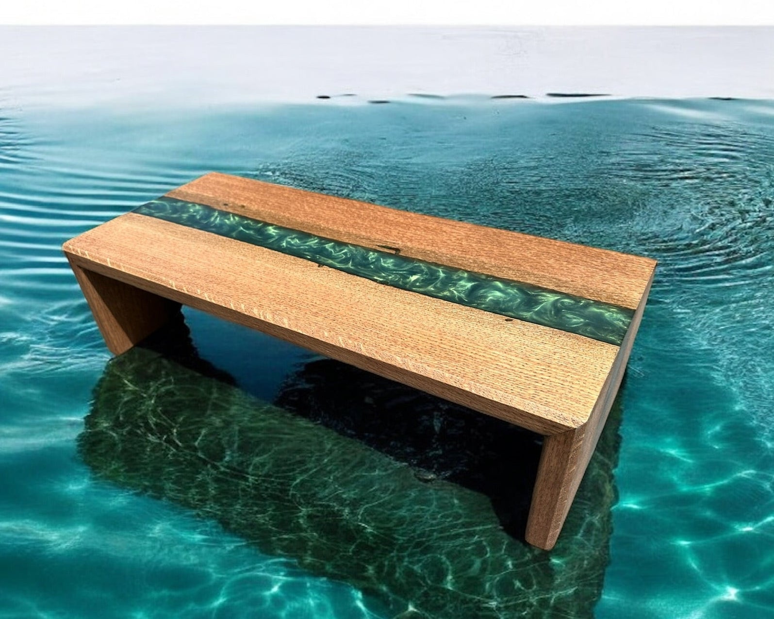 A rectangular wooden monitor stand with a green resin river partially submerged in clear turquoise water with rippling ripples around it.