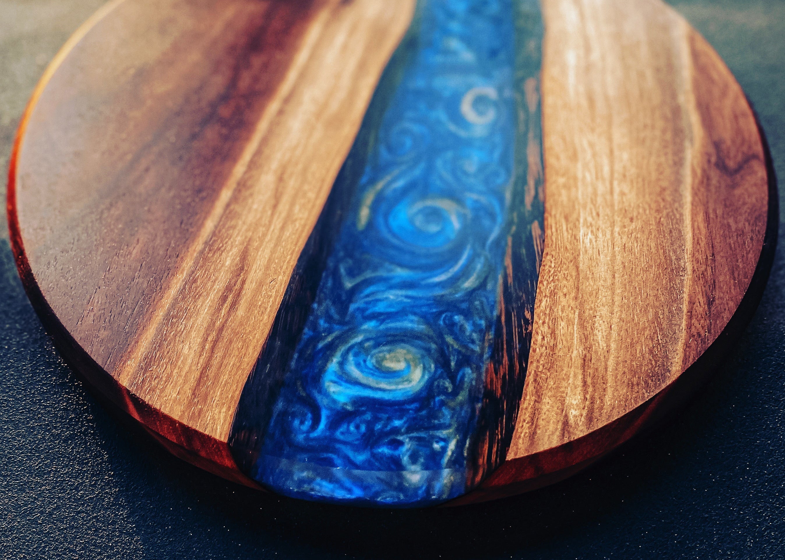 Round wooden serving board or tray with a vibrant blue resin river design running down the center, flanked by natural wood grain sides.