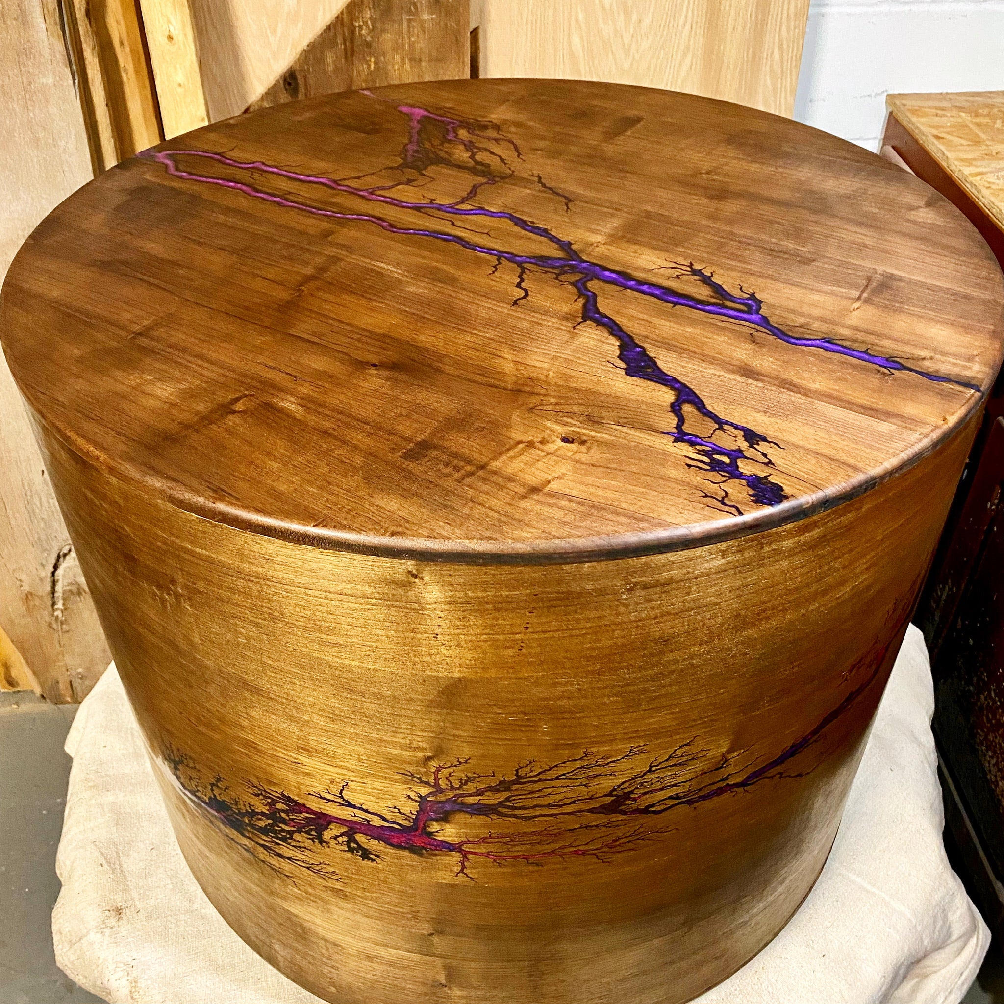 A round wooden walnut table with a purple resin fractal burn inlay resembling tree roots, shown on a white cloth in a workshop setting.