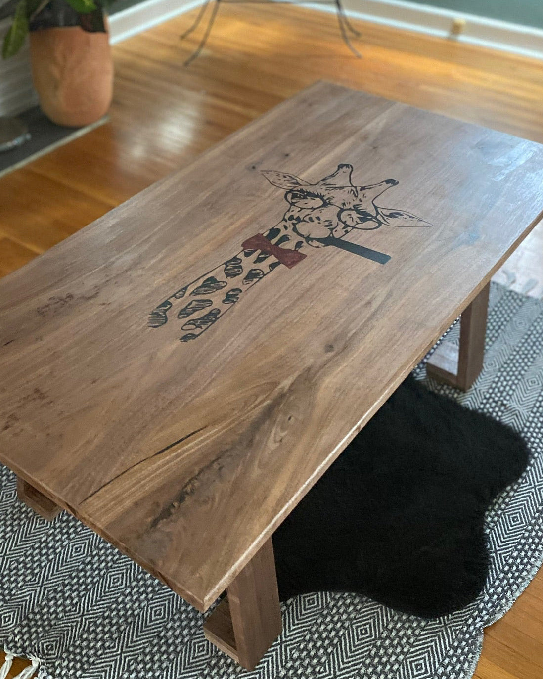 A rectangular wooden coffee table with a live edge and a giraffe resin inlay styled in a living room setting on a patterned rug over a hardwood floor.