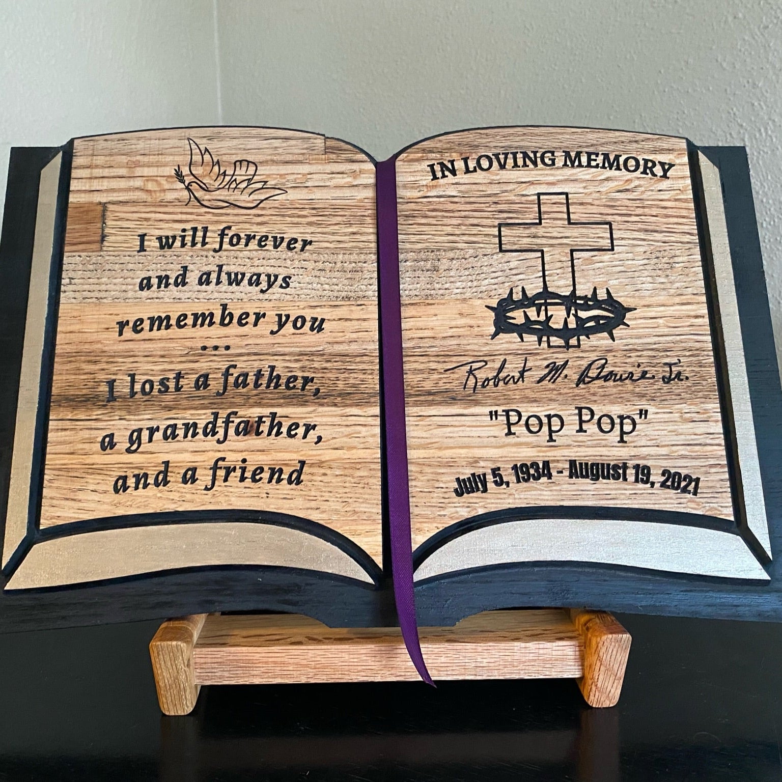 Wooden book-shaped memorial with engraved text on a plain background