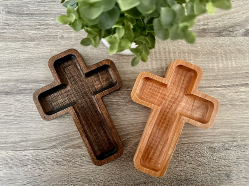 Two wooden cross-shaped trays on a wooden surface with a plant in the background.