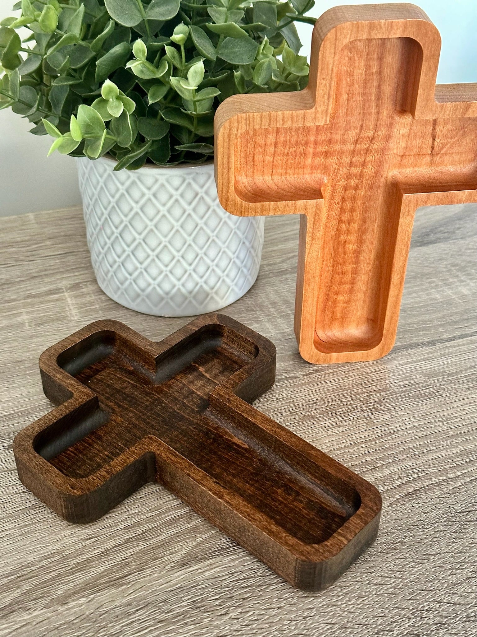 Wooden cross-shaped trays on a wooden surface with a potted plant in the background.