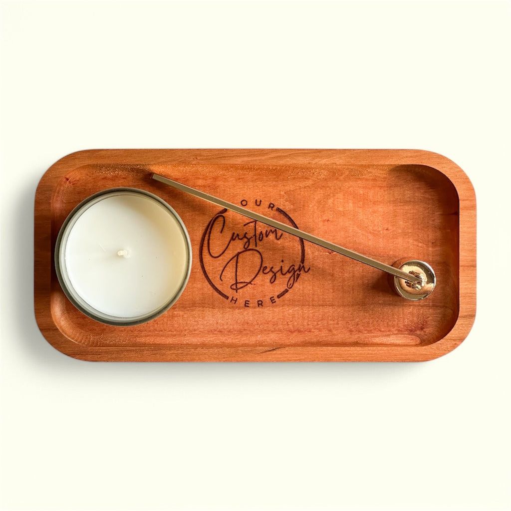 A rectangular wooden tray with rounded corners, featuring an engraved logo that reads 'your Custom Design Here' and a brass candlestick holding a white candle, photographed from above on a light cream background.