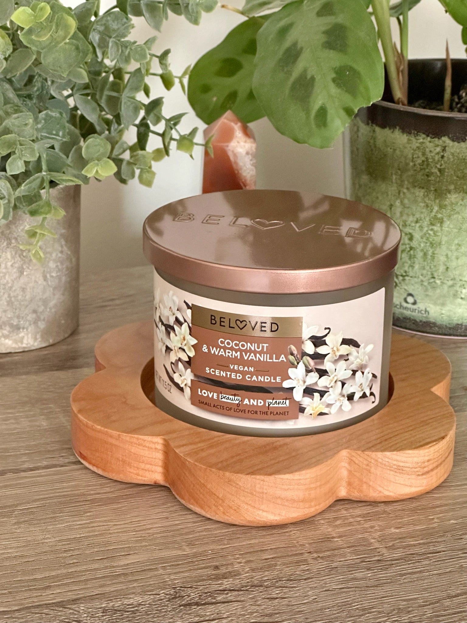 Beloved candle on a wooden flower coaster with plants in the background