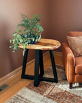 A rustic live-edge wood end table with a black metal A-frame base, styled in a living room next to an orange armchair on a patterned rug. The brand name 'Third Eye Creation Co.