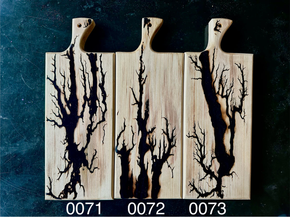 Three rectangular wooden cutting boards with integrated handles, arranged side by side on a dark textured background. Each board features a sparkly black tree style design running vertically.