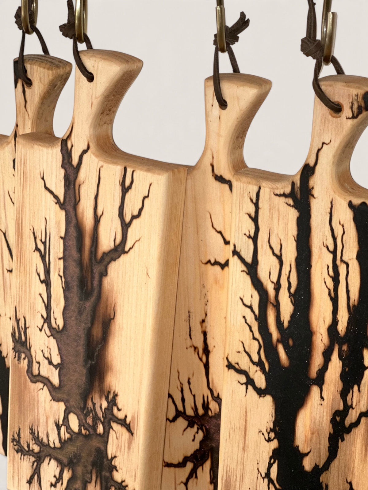 A close-up of several natural wood cutting boards with dark brown to black burnt tree branch patterns, hanging from metal hooks.