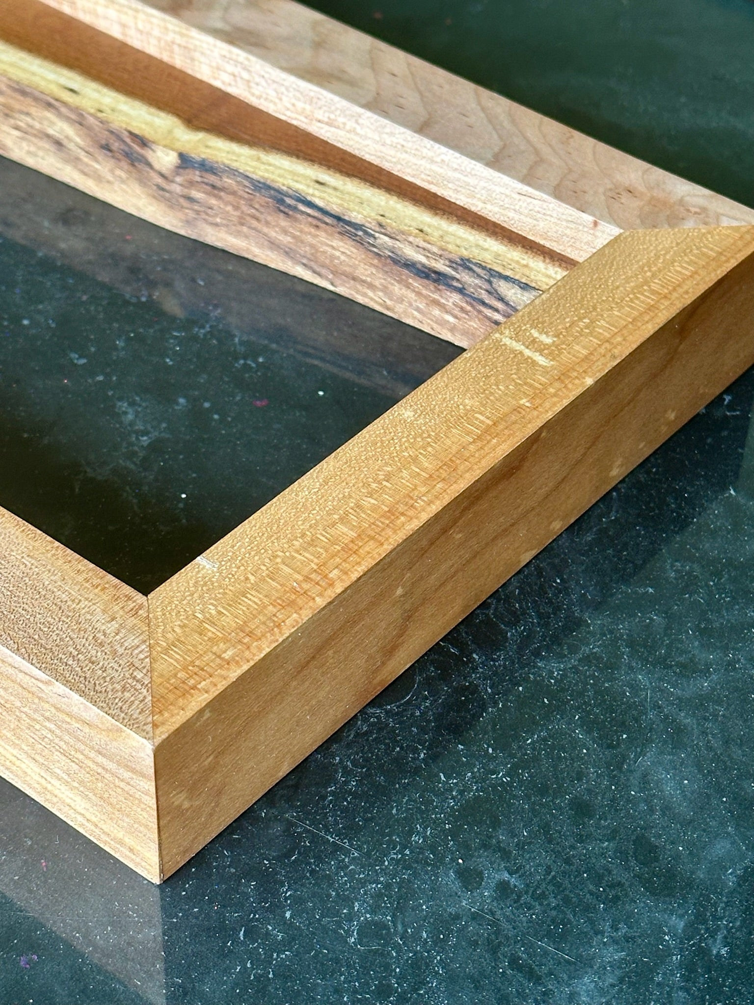 Close-up of a light natural wood picture frame corner with a dark green marble surface underneath.