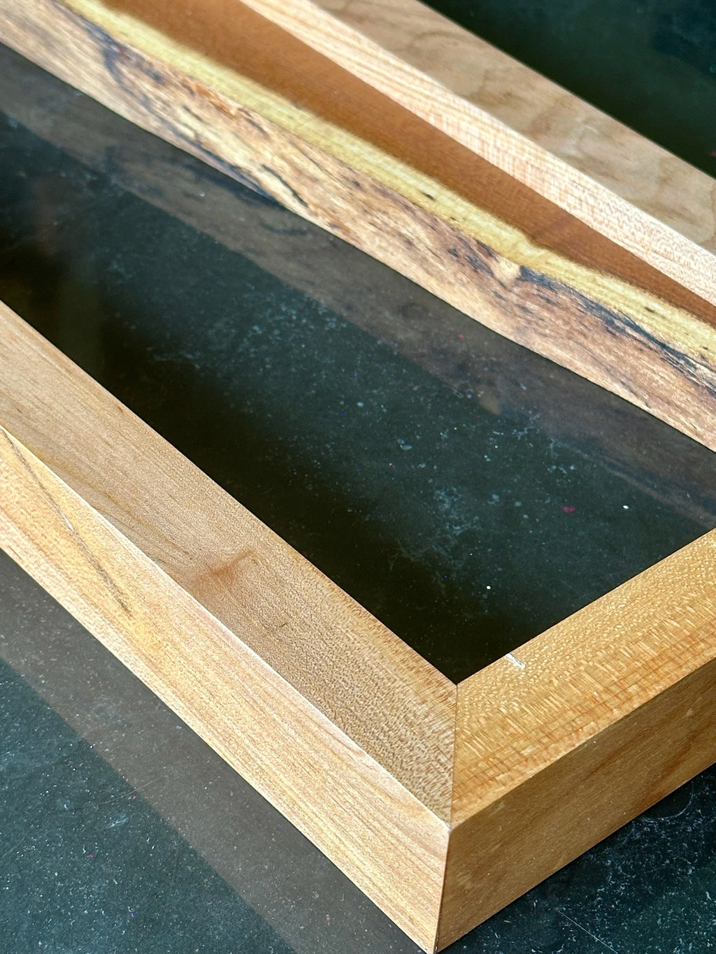 Close-up of a wooden picture frame with a live-edge natural wood top, showing the grain and dark recessed interior.