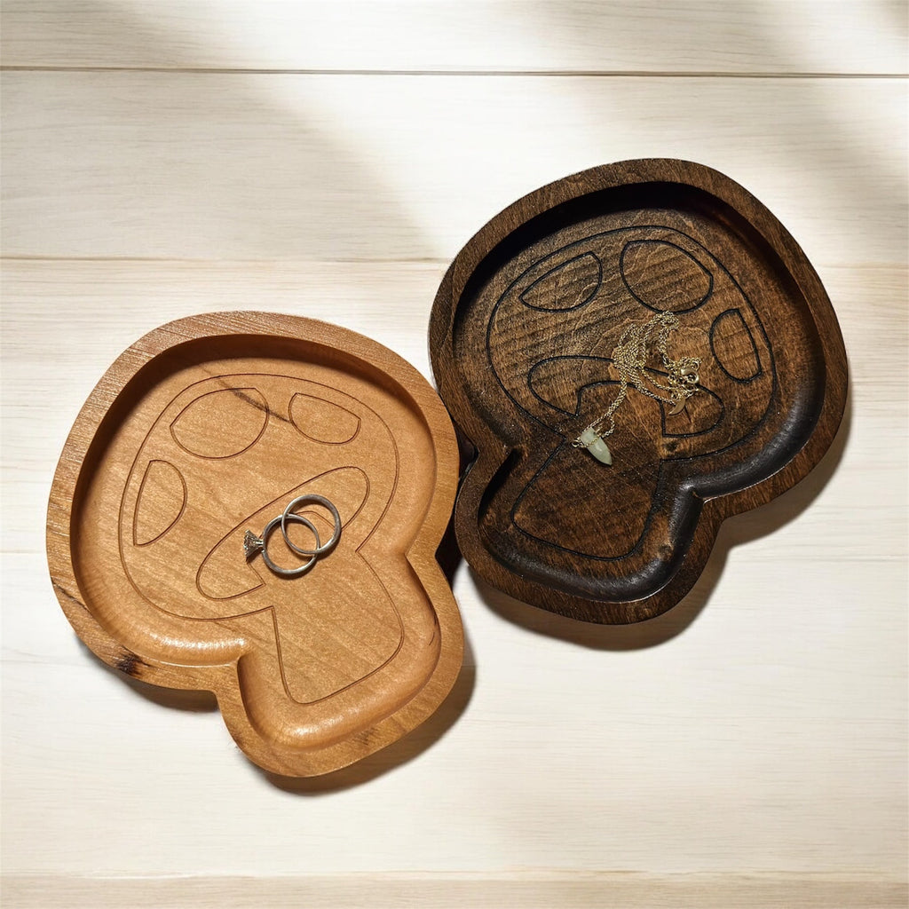 Two wooden mushroom jewelry trays with a ring and necklace on a light wood surface