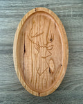 An oval wooden tray with a carved deer head design, displayed on a gray wood-textured background.