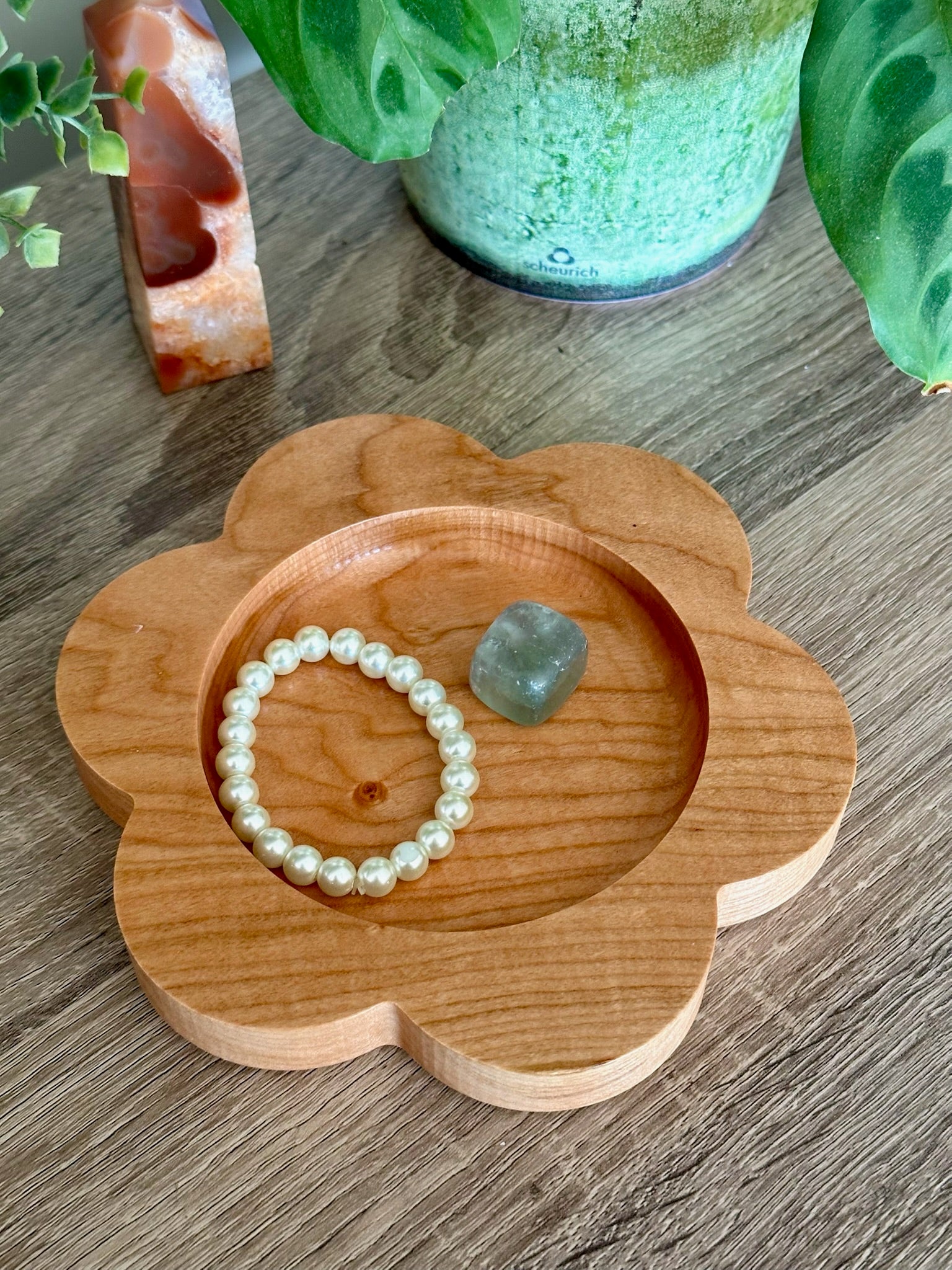 Wooden flower-shaped tray with a pearl bracelet and green crystal on a wooden surface.