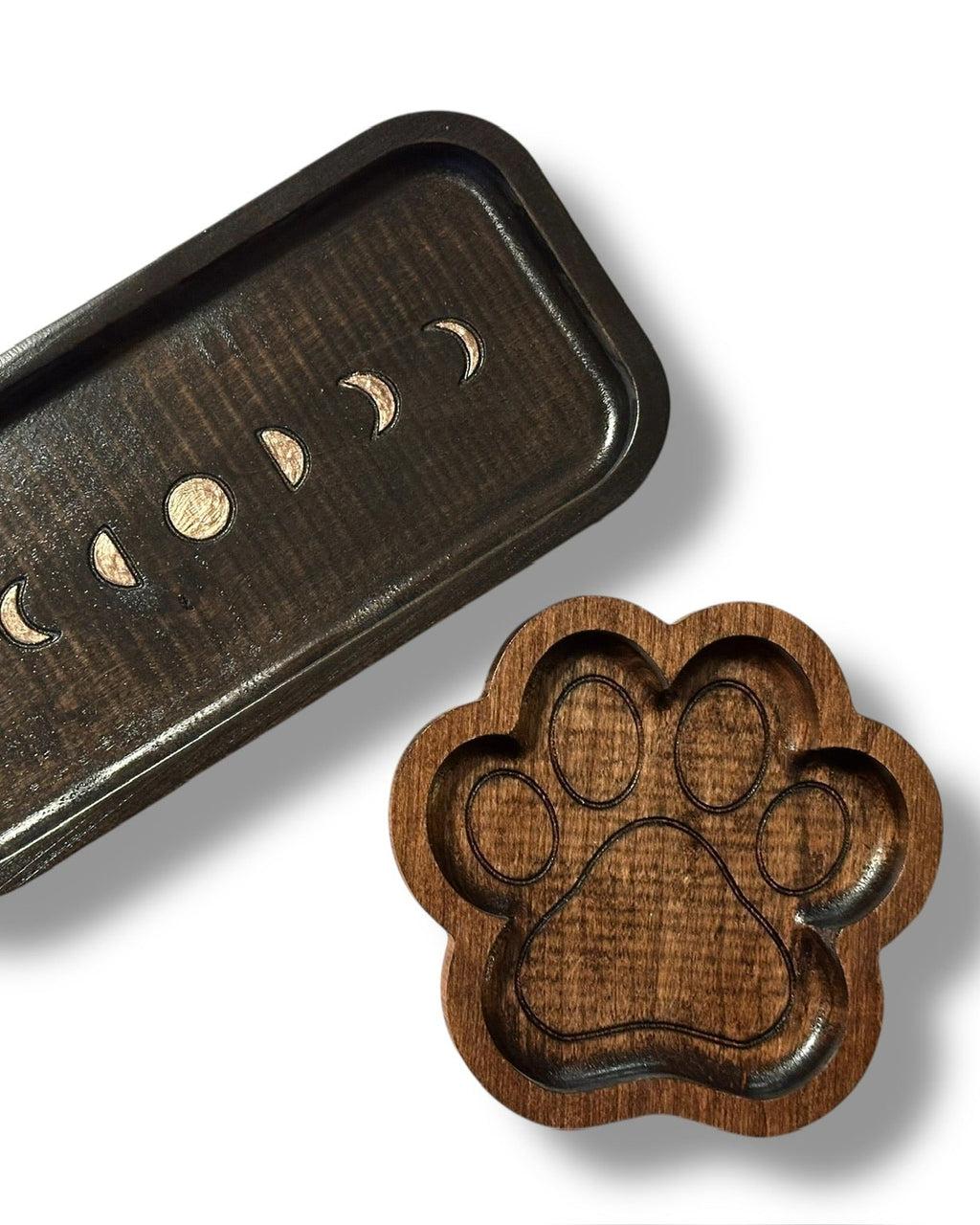 A dark brown wooden tray with a moon phase design and a matching paw-shaped tray displayed on a clean white background.