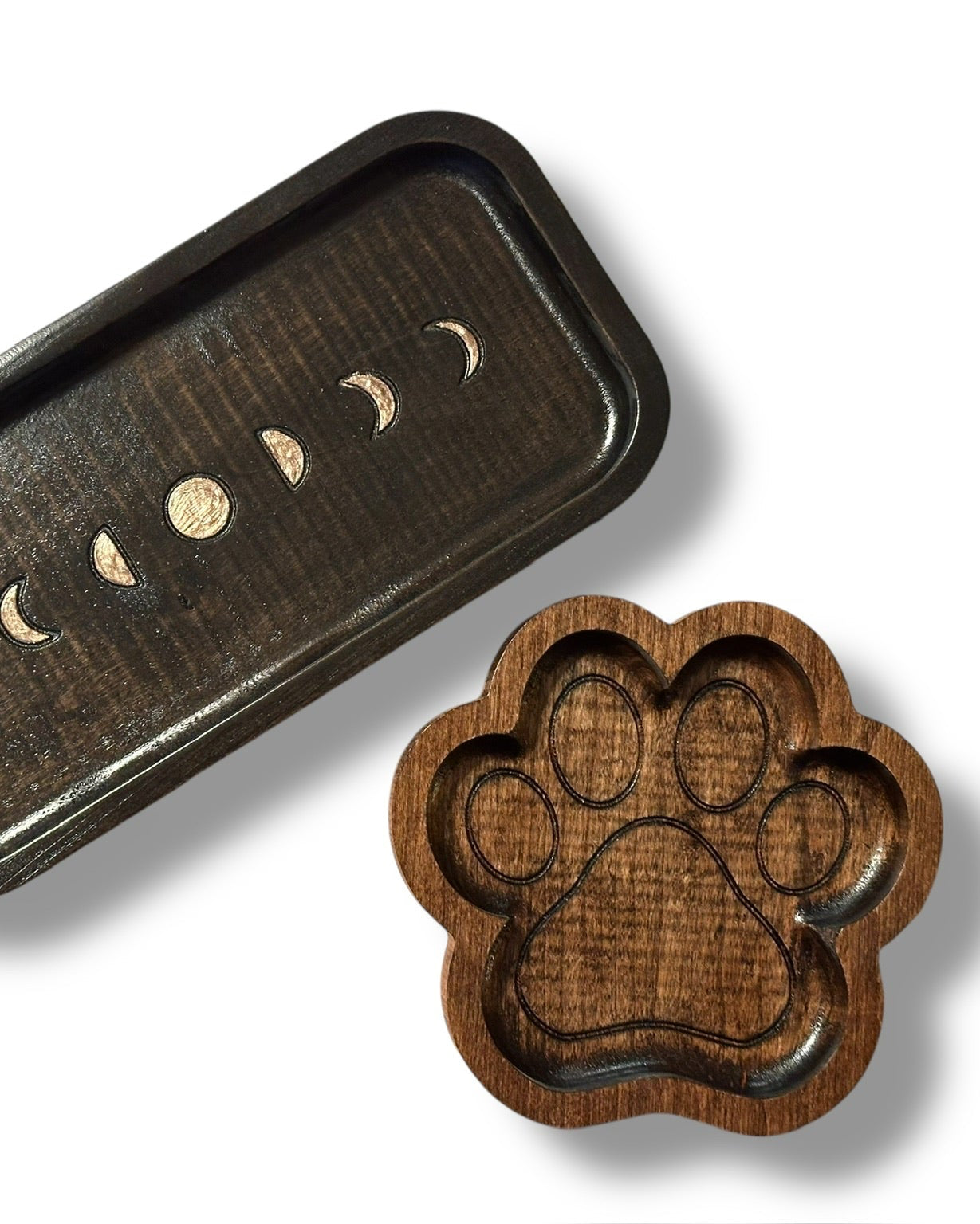 A dark brown wooden tray with a moon phase design and a matching paw-shaped tray displayed on a clean white background.