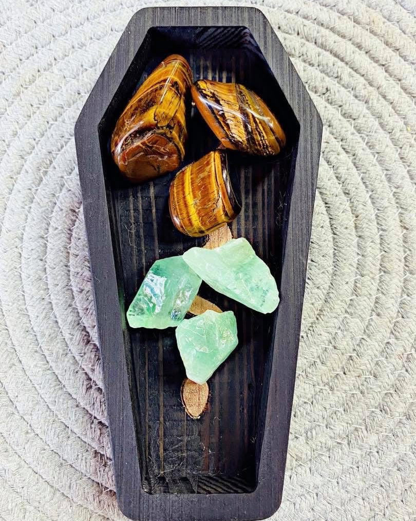Decorative display of amber and green crystals in a black coffin-shaped container on a textured white background.
