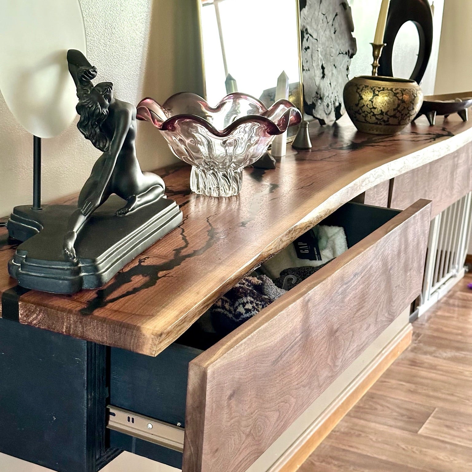 A rustic floating walnut console table with a live-edge top and an open drawer, styled with decorative objects in a home interior setting.